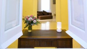 Una habitación con una pared amarilla, un escritorio de madera con un florero de flores, un sofá marrón y una lámpara blanca.