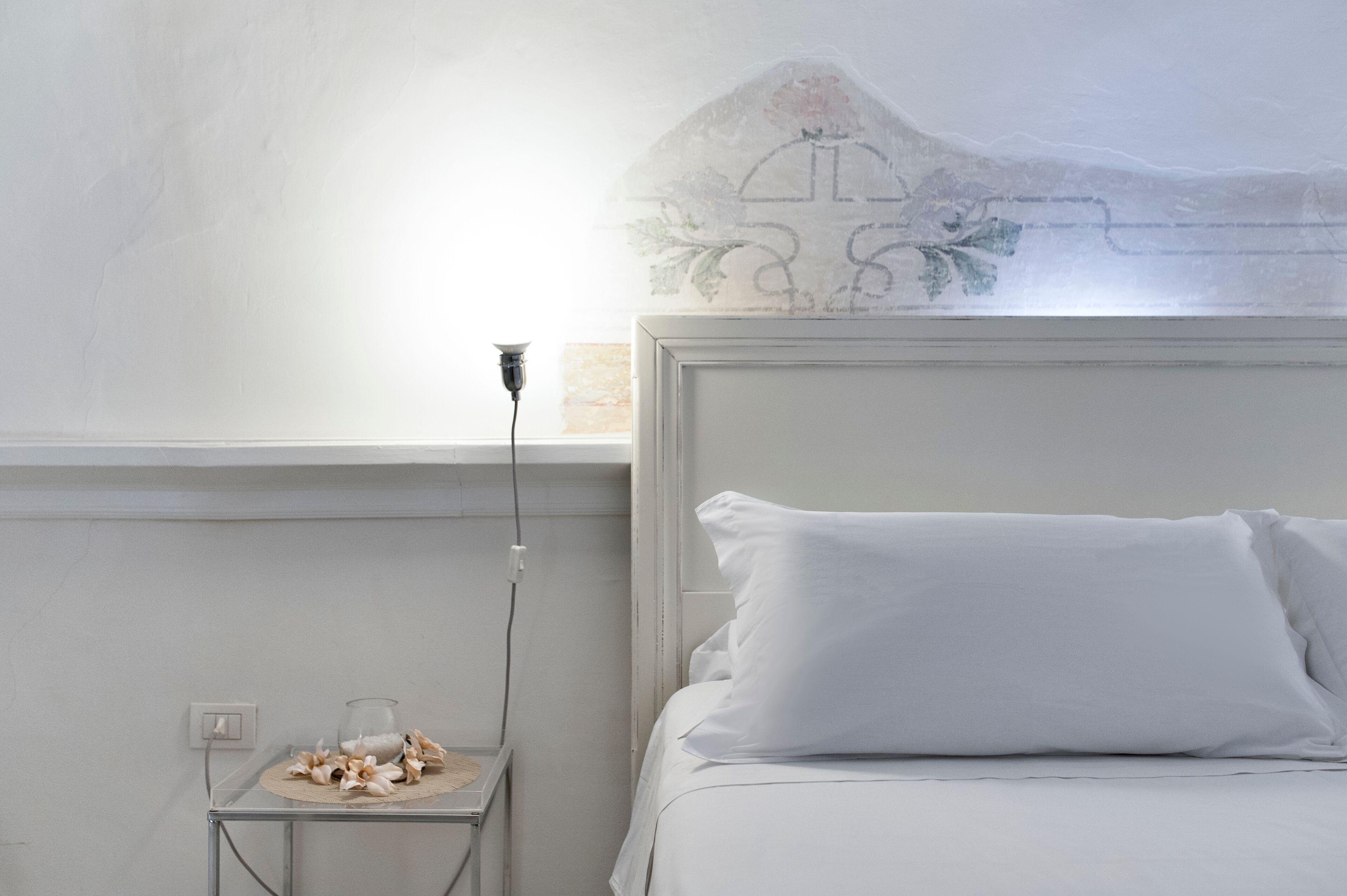 Ein Schlafzimmer mit einem Bett, einem Nachttisch mit Lampe und einer Wand mit dekorativem Design.