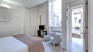 Un dormitorio moderno con cama, televisor, sillón y balcón con vistas a la calle.