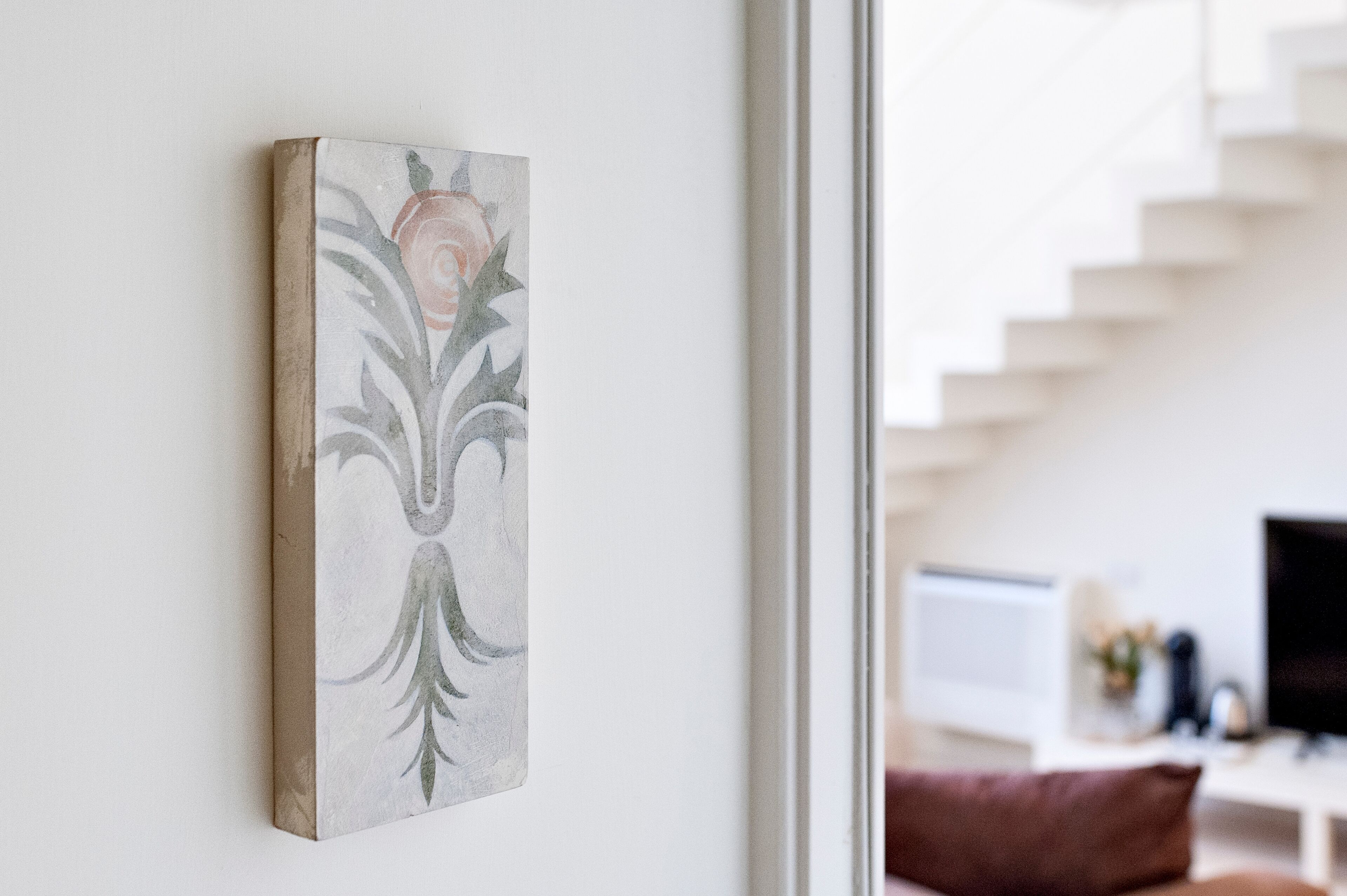 Une œuvre d’art encadrée accrochée au mur, un escalier et une pièce avec un téléviseur et une plante.