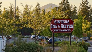 A Sisters Inn & Suites entrance sign with a parking lot and trees in the background. - Sisters Inn And Suites (Sisters)