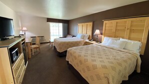 A hotel room with two beds, a desk, a chair, a television, and a window with curtains. - Sisters Inn And Suites (Sisters)
