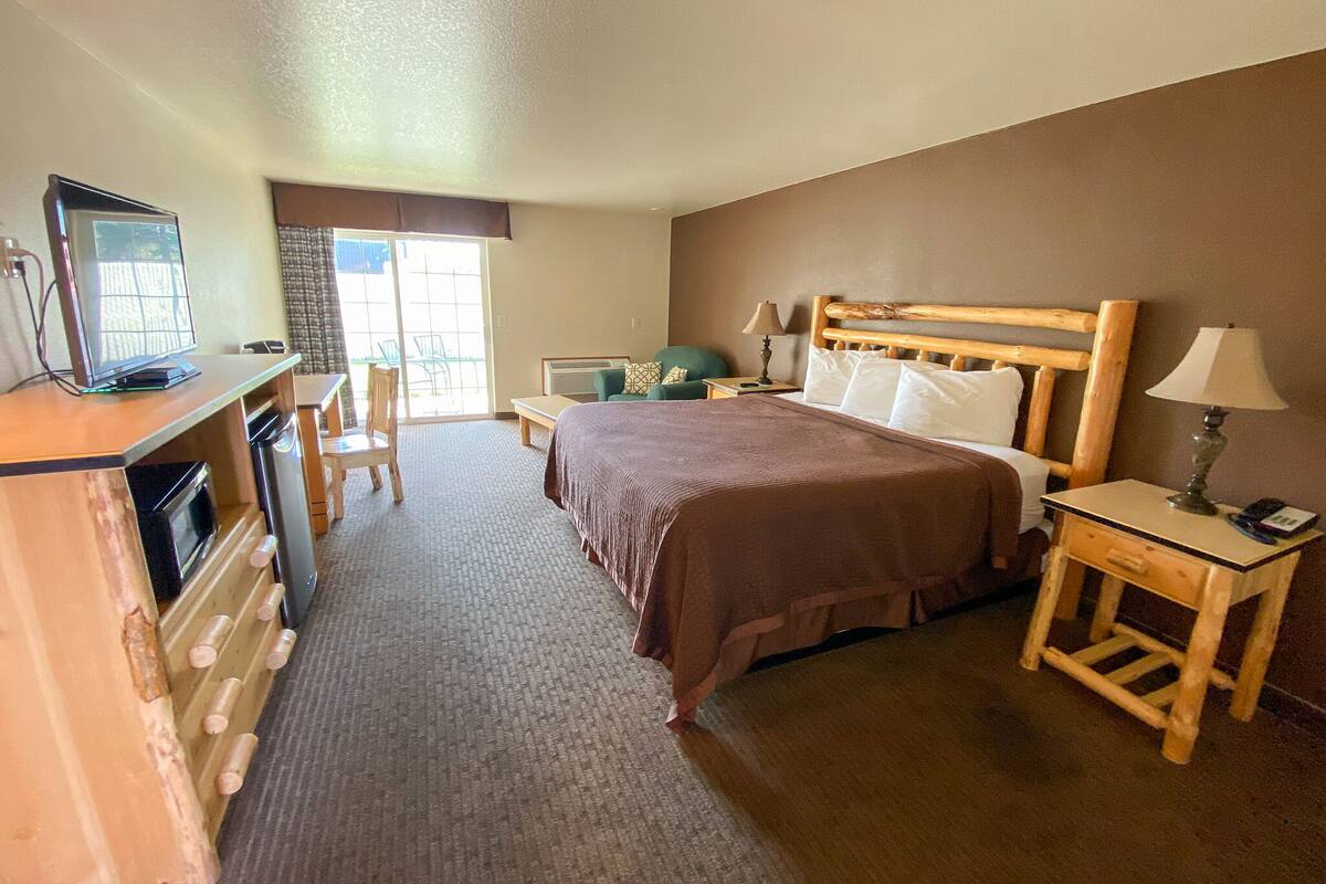 Ein Hotelzimmer mit Bett, Schreibtisch mit Computer, Stuhl, Lampe und Fenster.