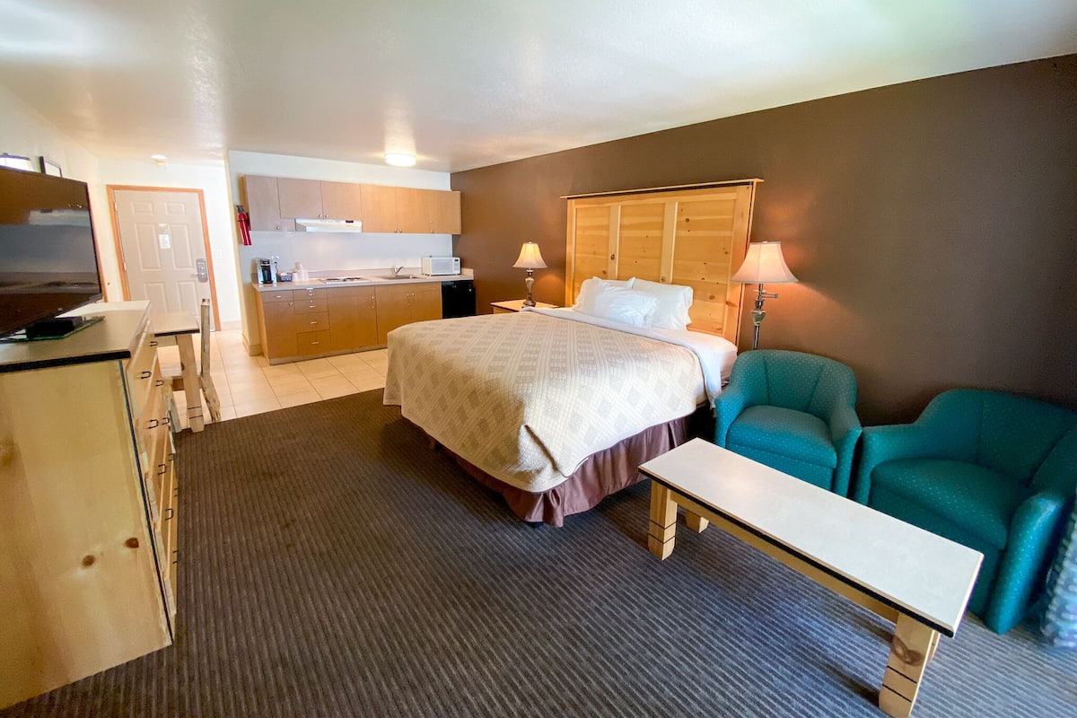 Ein Hotelzimmer mit Bett, Schreibtisch, Stuhl, Küchenzeile und Fernseher.