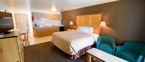 Una habitación de hotel con cama, escritorio, silla, kitchenette y televisión.