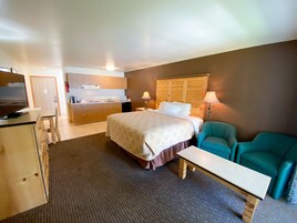 Una habitación de hotel con cama, escritorio, silla, kitchenette y televisión.