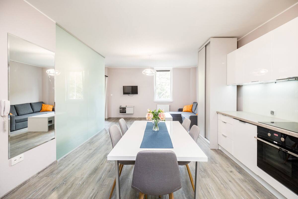 Een moderne keuken met witte kasten, een zwarte oven en een eethoek met een witte tafel en stoelen.