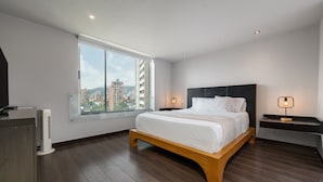 A modern bedroom with a large window, a wooden bed frame, and a nightstand with a lamp.