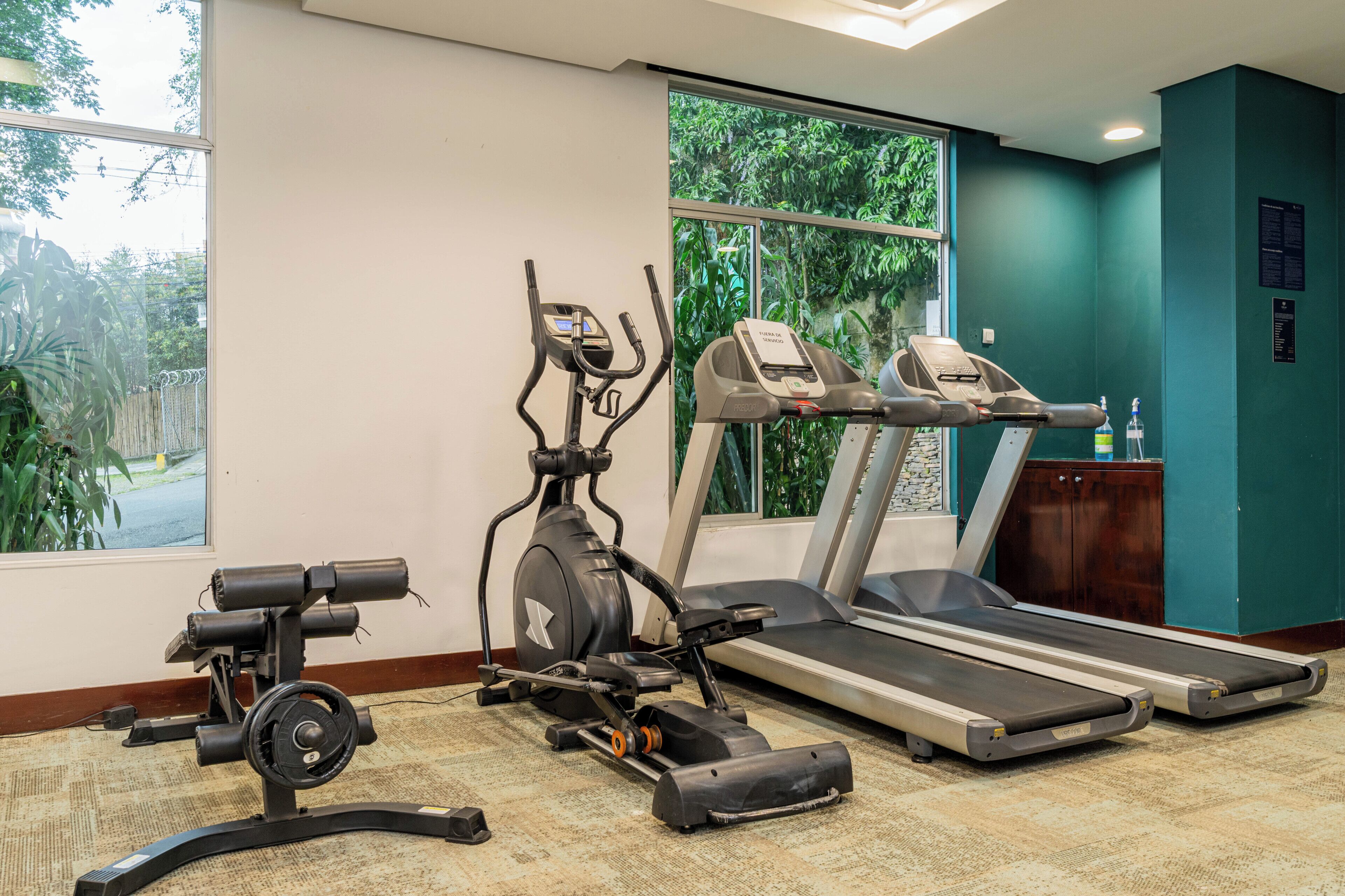 A gym with cardio equipment, a weight bench, and a water bottle on a counter.