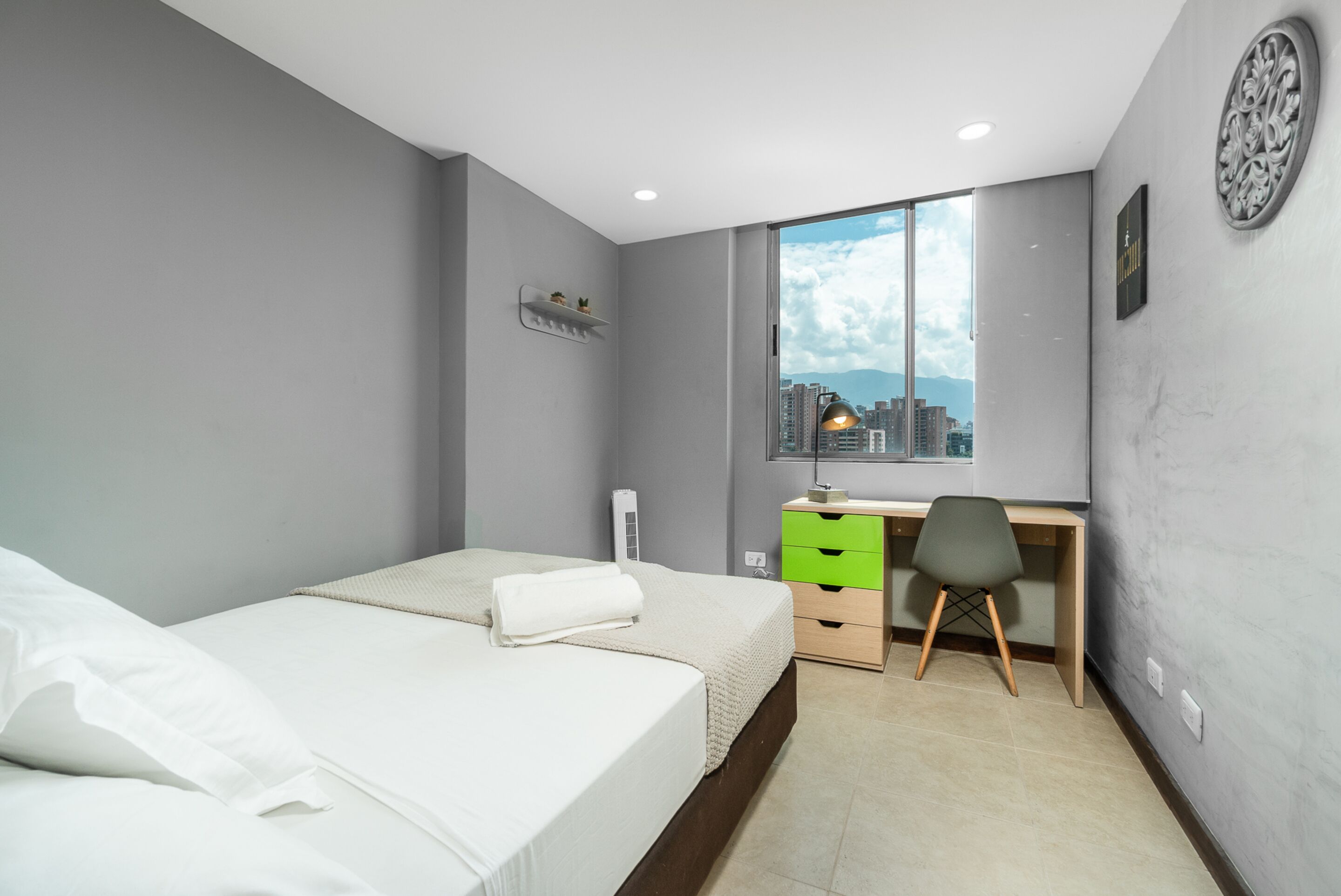 Un dormitorio moderno con cama, escritorio y ventana con vista a la ciudad.