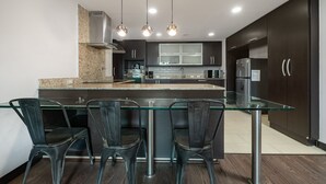 A modern kitchen with dark cabinets, a glass island, and three pendant lights.