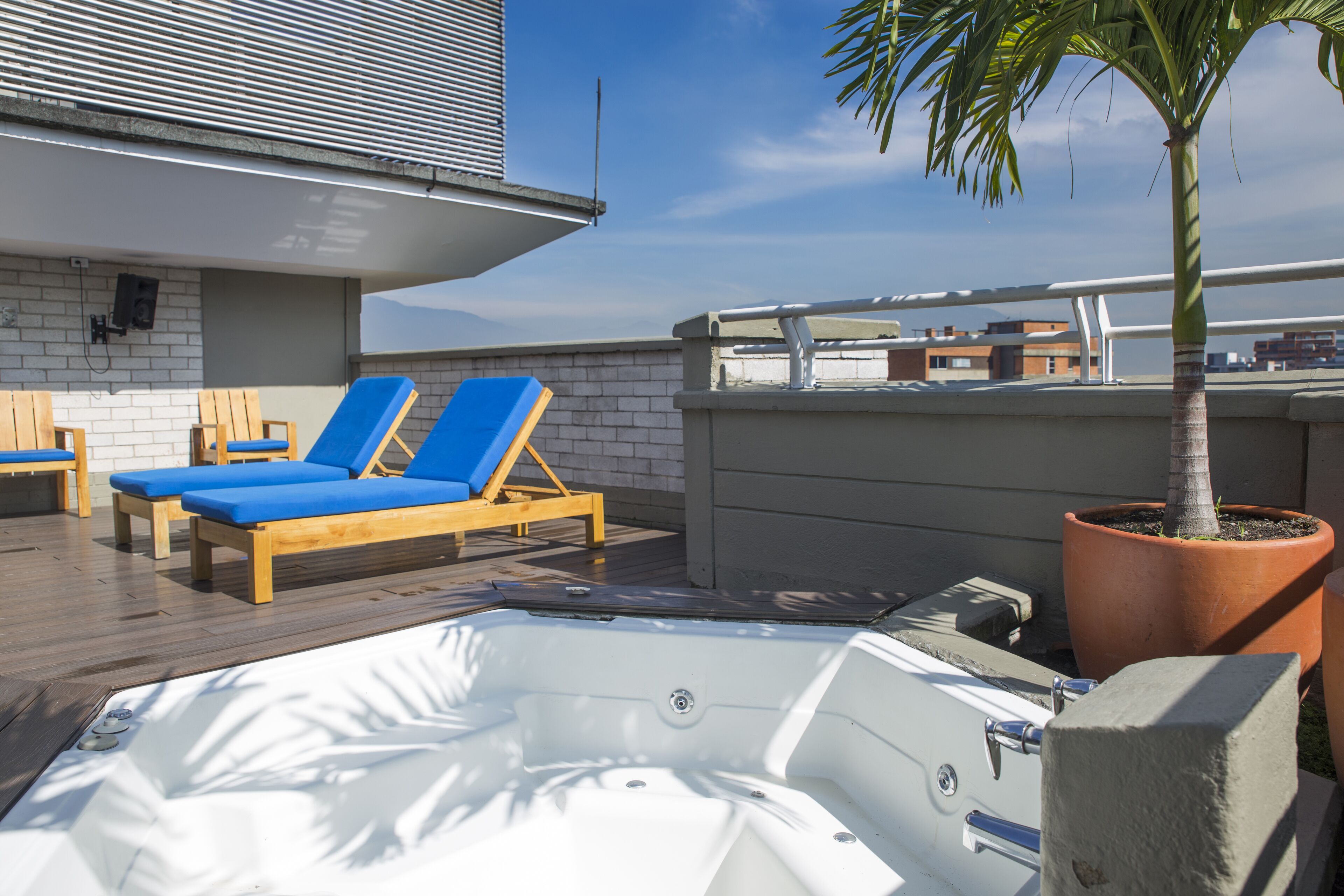 A rooftop lounge area with a hot tub, wooden lounge chairs, and a potted palm tree.