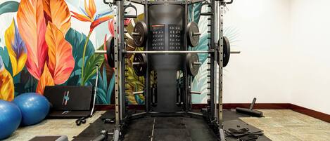 A gym with a weightlifting station, exercise balls, and a colorful mural.
