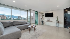 A modern living room with a grey sectional sofa, a small round table, and a large window offering a city view.