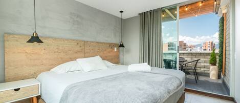 A modern hotel room with a large bed, wooden headboard, and a balcony with a city view.