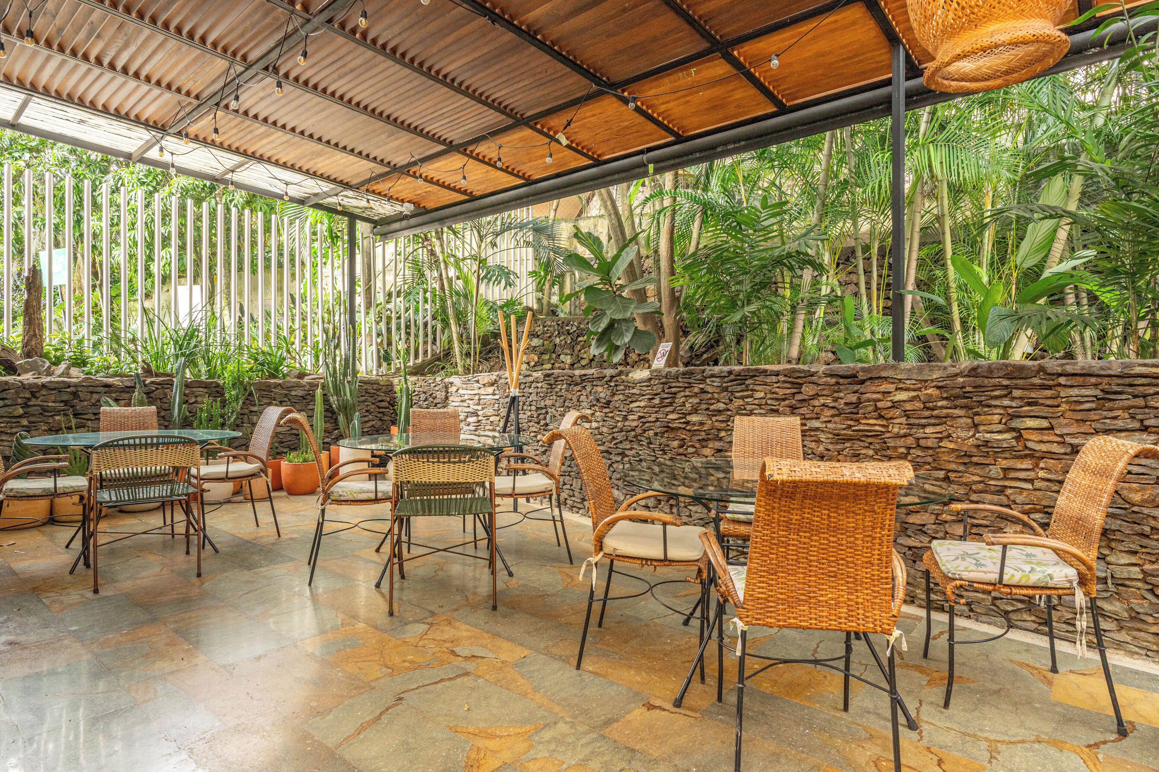 Un espace extérieur aménagé en terrasse, avec des meubles en osier, des murs en pierre et des plantes tropicales.