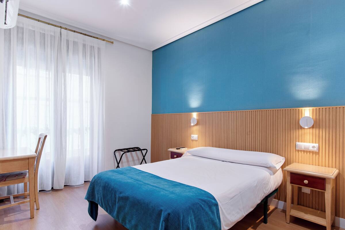 A hotel room with a bed, bedside tables, a chair, and a desk.