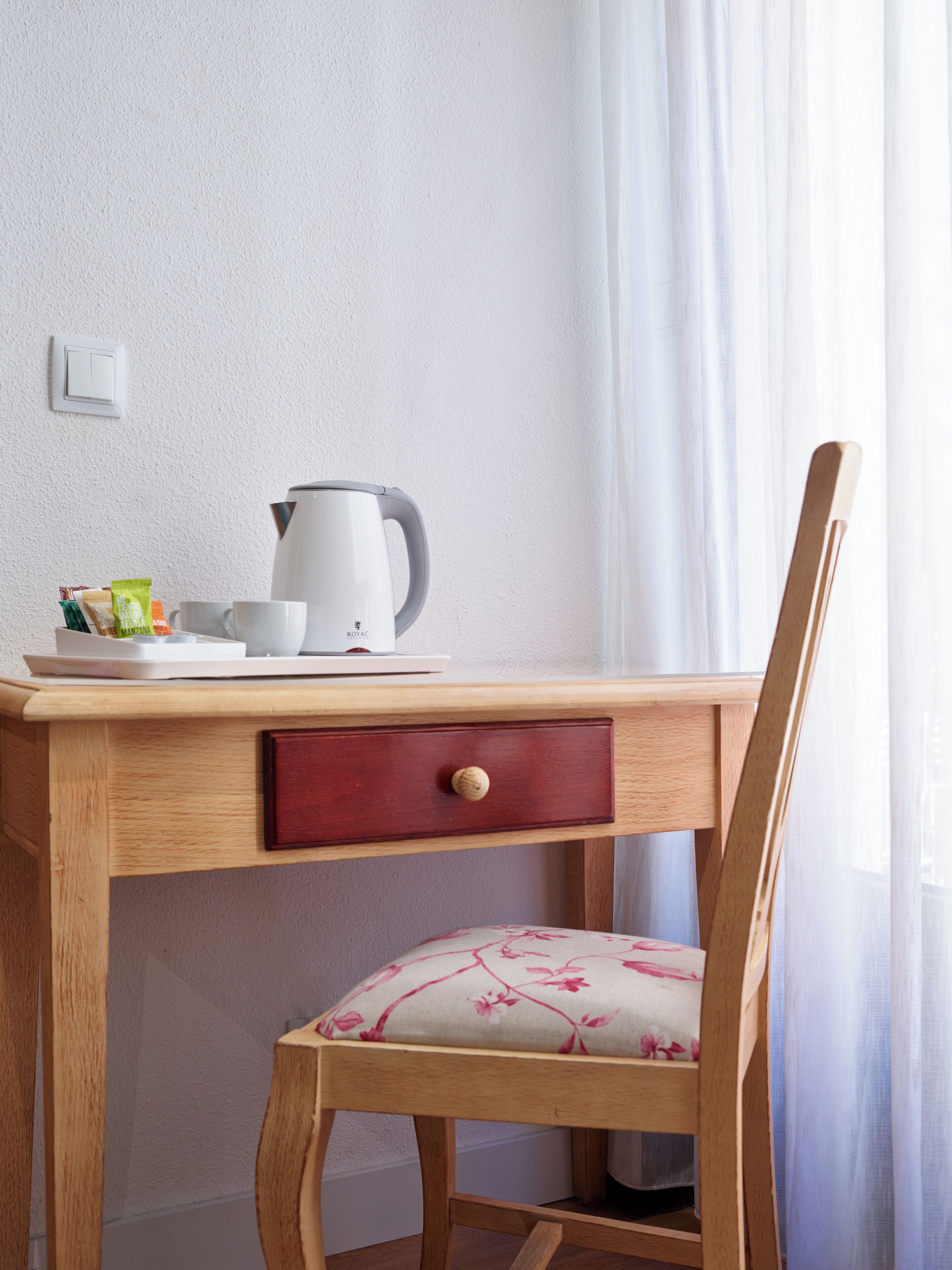 A wooden desk with a red drawer, a white kettle, and a cup on it.