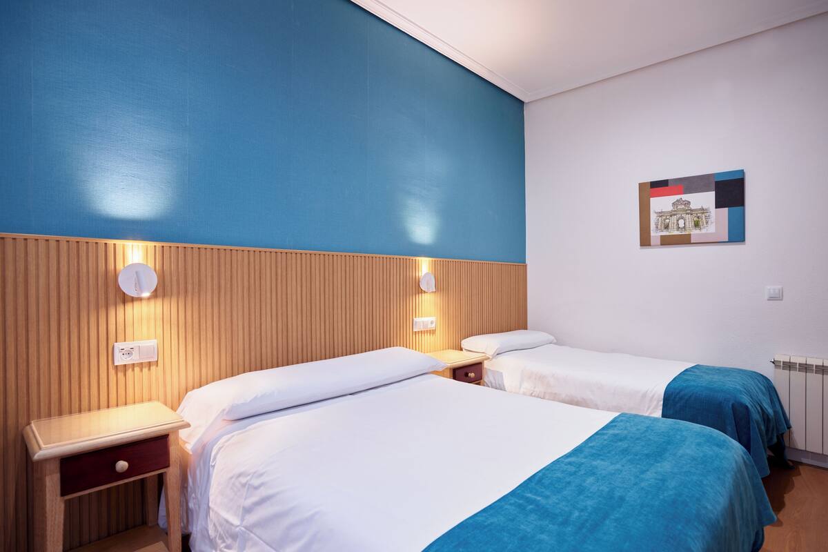 A hotel room with two beds, wooden headboards, and a blue accent wall.