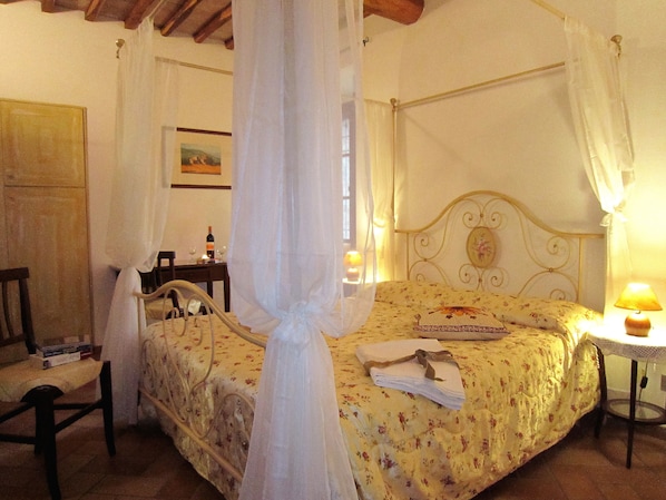 Un dormitorio con cama con dosel, una mesita de noche con lámpara y una silla.