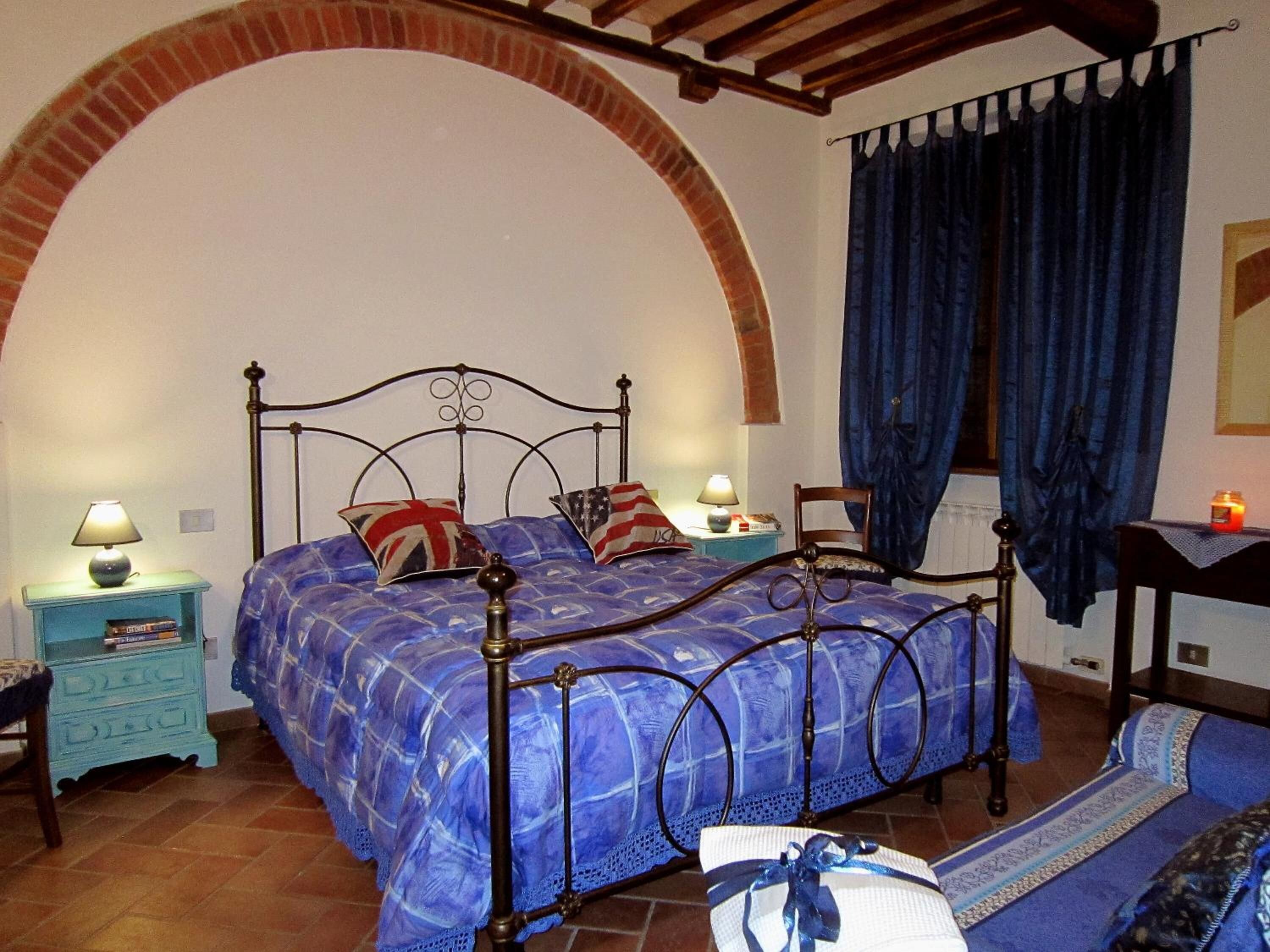 A bedroom with a bed, two bedside tables, a nightstand, a window with curtains, and a small table with a candle.