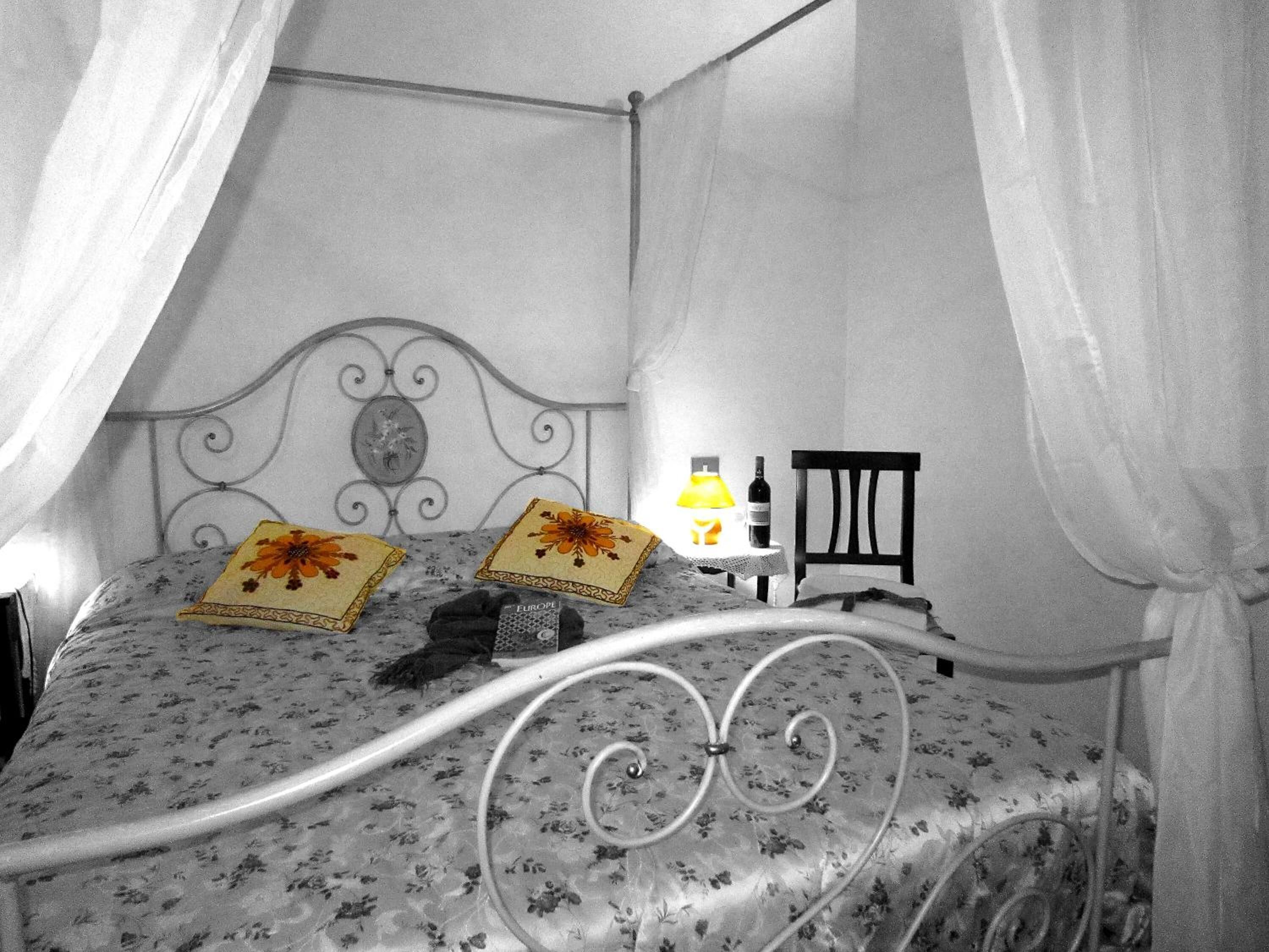 A bed with a metal frame, floral bedspread, and two pillows with floral designs. There is a nightstand with a lamp and a bottle.