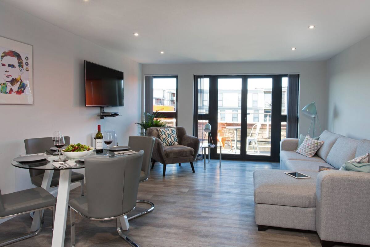 A modern living room with a dining area, a sofa, a TV, and a balcony with a view of the city.