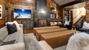 A cozy log cabin interior with a fireplace, comfortable seating, and a television.