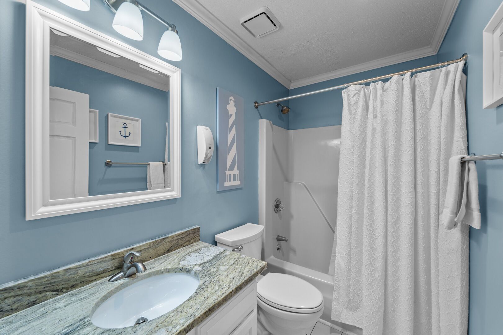A bathroom with a marble sink, white toilet, and a walk-in shower with a white shower curtain.
