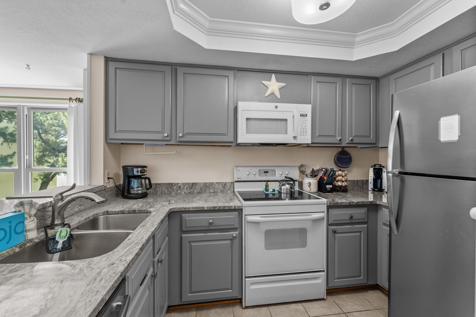 A kitchen with gray cabinets, a stainless steel refrigerator, a microwave, a stove, and a coffee maker.