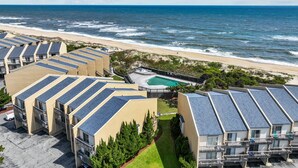 A coastal hotel with multiple buildings featuring rooftop solar panels, a pool, and a beach view.