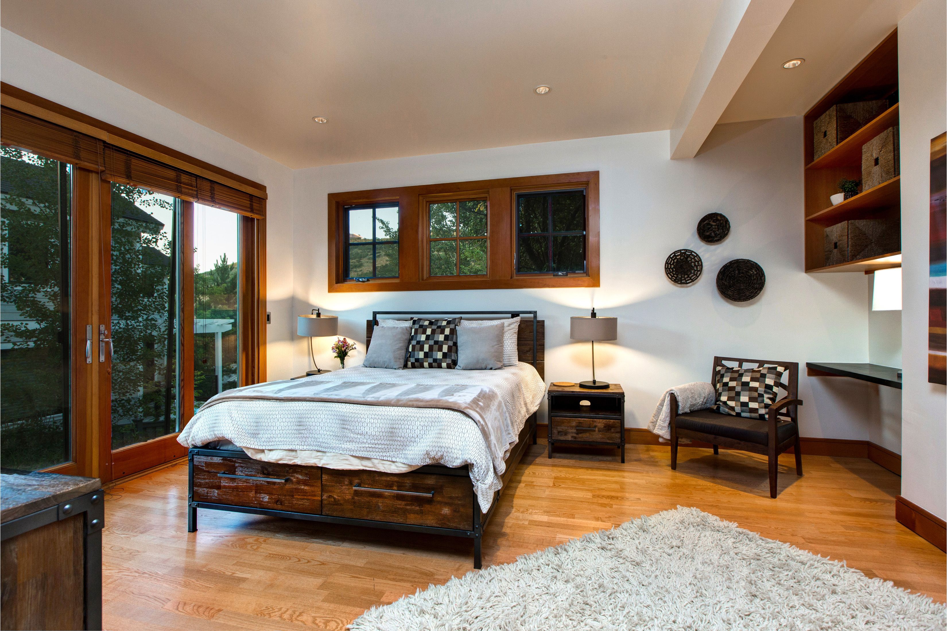 A bedroom with a large bed, wooden floor, and a view through a sliding door.