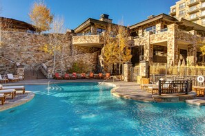 A pool area with lounge chairs and a stone building with balconies. - Abode at St. Regis (Park City)