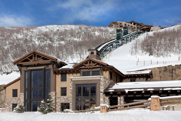 A large lodge with a ski lift, stone and wood exterior, and snow-covered surroundings. - Abode at St. Regis (Park City)