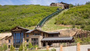 Un chalet de montagne doté d'un télésiège, d'une architecture en pierre et en bois, et offrant une vue sur la forêt environnante.