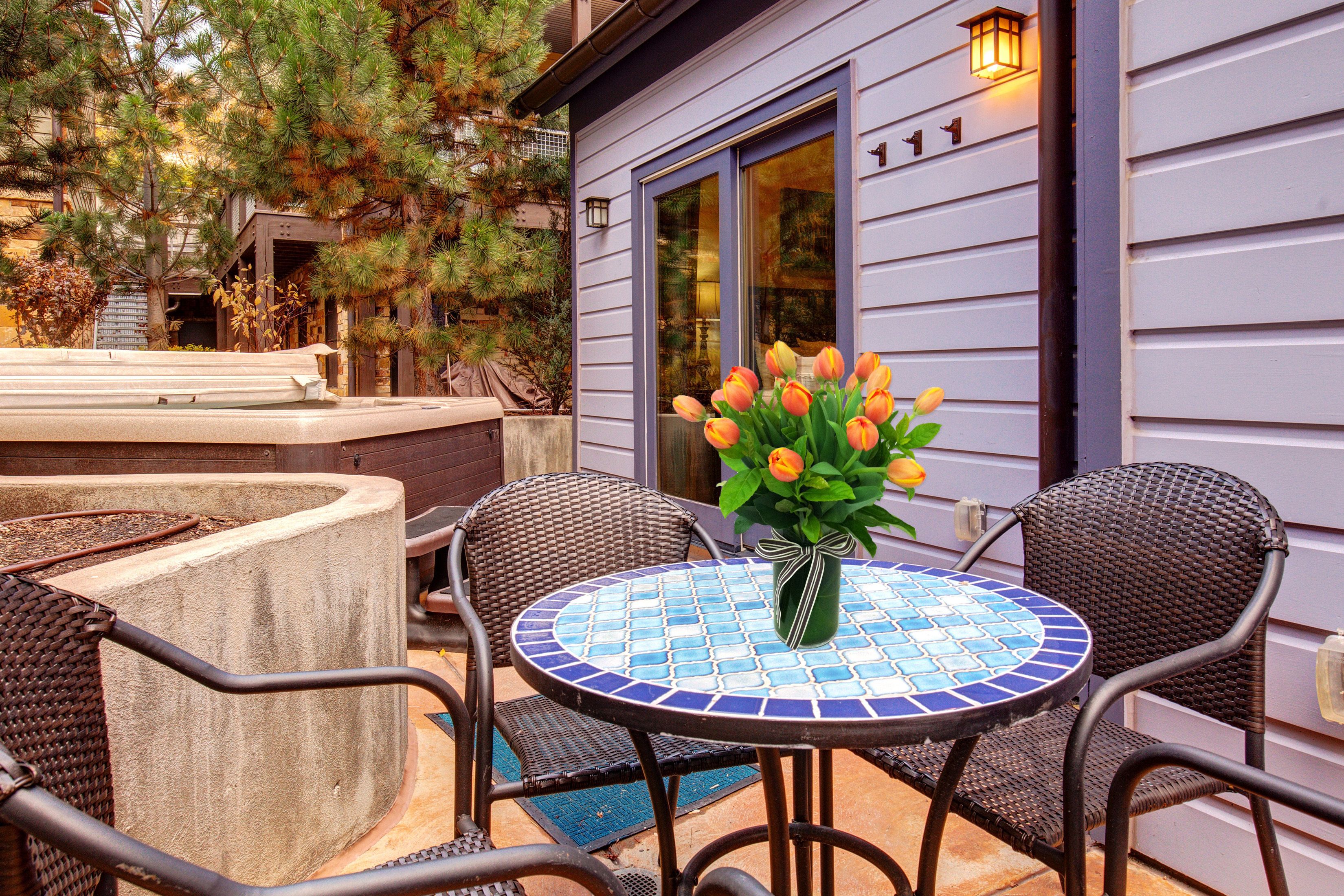 Eine Terrasse im Freien mit einem runden Tisch, zwei Korbstühlen und einer Vase mit orangefarbenen Tulpen.