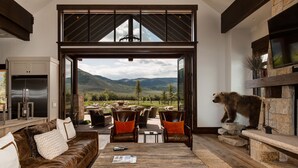 A spacious living area with a large window overlooking a mountainous landscape, furnished with a leather sofa, chairs, and a coffee table. - Abode at Twilight Ranch (Oakley)