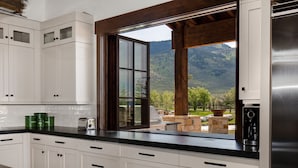A kitchen with white cabinets, a black countertop, and a large window overlooking a mountainous landscape. - Abode at Twilight Ranch (Oakley)