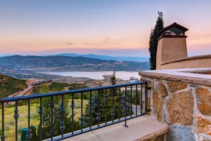A balcony with a stone wall and metal railing overlooking a valley with a lake and distant mountains. - Abode in Deer Crest (Park City)