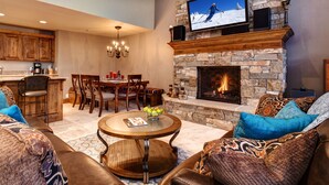 Una sala de estar acogedora con chimenea de piedra, un televisor montado encima y un comedor con mobiliario de madera.
