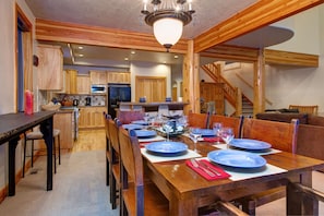 A wooden dining table set with blue plates, a chandelier, and a staircase leading to another level. - Abode on Nakoma (Park City)