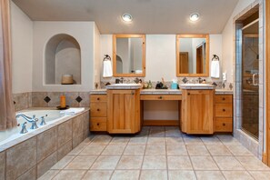 A bathroom with two sinks, wooden cabinets, a bathtub, and a shower area.