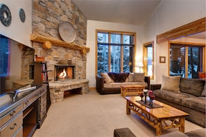 A cozy living room with a stone fireplace, large windows, and comfortable seating. - Abode on Nakoma (Park City)