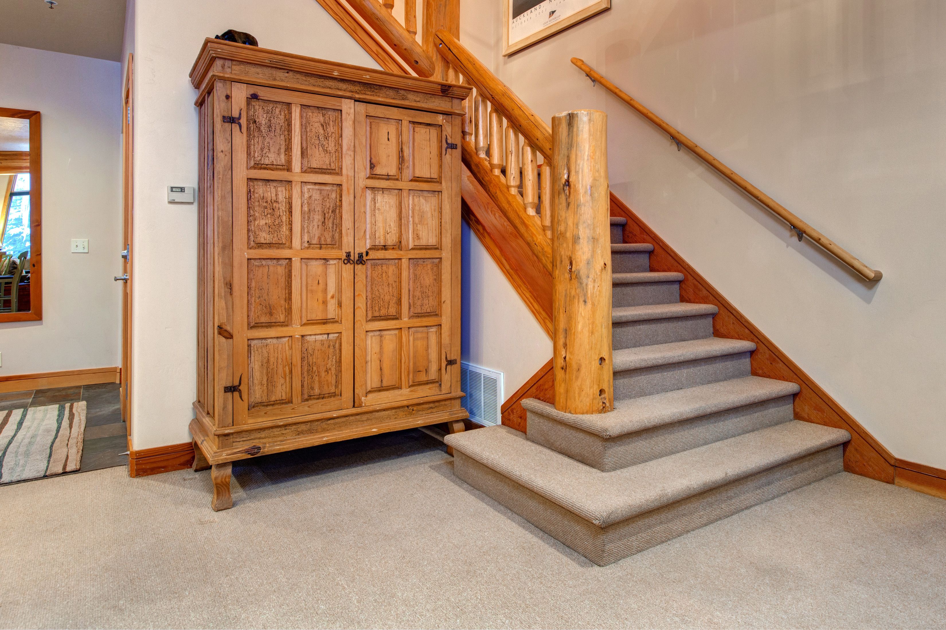 A wooden staircase with carpeted steps and a wooden handrail, leading to a landing with a large wooden cabinet.