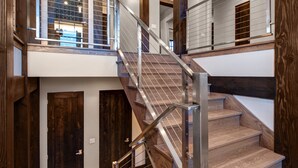 Eine mehrstufige Holztreppe mit Metallgeländern, die zu einer zweiten Etage mit Blick auf einen Raum mit einem großen Fenster führt.