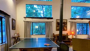 Een tafeltennistafel in een kamer met grote ramen, een open haard en een gezellige zithoek.