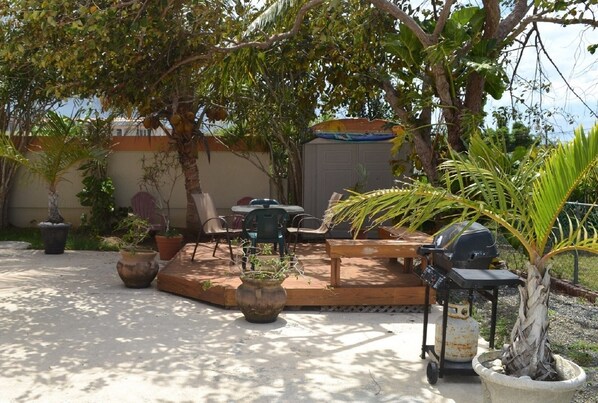 An outdoor patio area with a wooden deck, several potted plants, a grill, and outdoor seating.