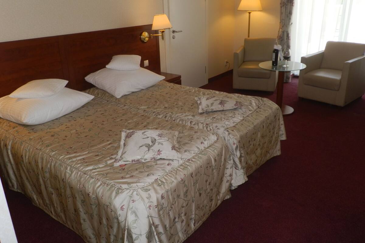 A hotel room with a large bed, two bedside lamps, a chair, and a small table.