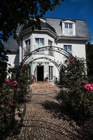 Ein zweistöckiges Haus mit weißer Fassade, einem schwarzen Dach und einer kreisförmigen Auffahrt zum Eingang.
