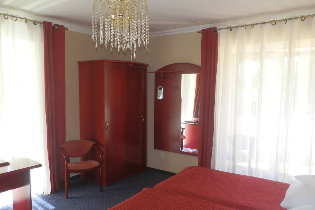 A hotel room with a bed, a desk, a chair, a wardrobe, and a chandelier.